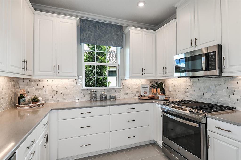 A kitchen features white cabinets, stainless steel appliances, a gray countertop, and a tiled backsplash — 13300 SANTINI CIRCLE, ENGLEWOOD, FL
