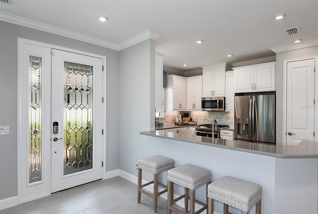 A kitchen with white cabinets and stainless steel appliances overlooks a breakfast bar with stools — 13300 SANTINI CIRCLE, ENGLEWOOD, FL