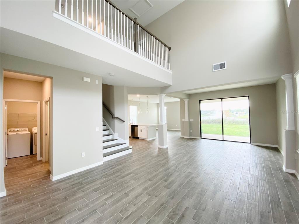 A spacious living area features high ceilings, wood-look tile flooring, a staircase, and sliding glass doors — 2307 KESTREL PERCH PLACE, WINTER PARK, FL