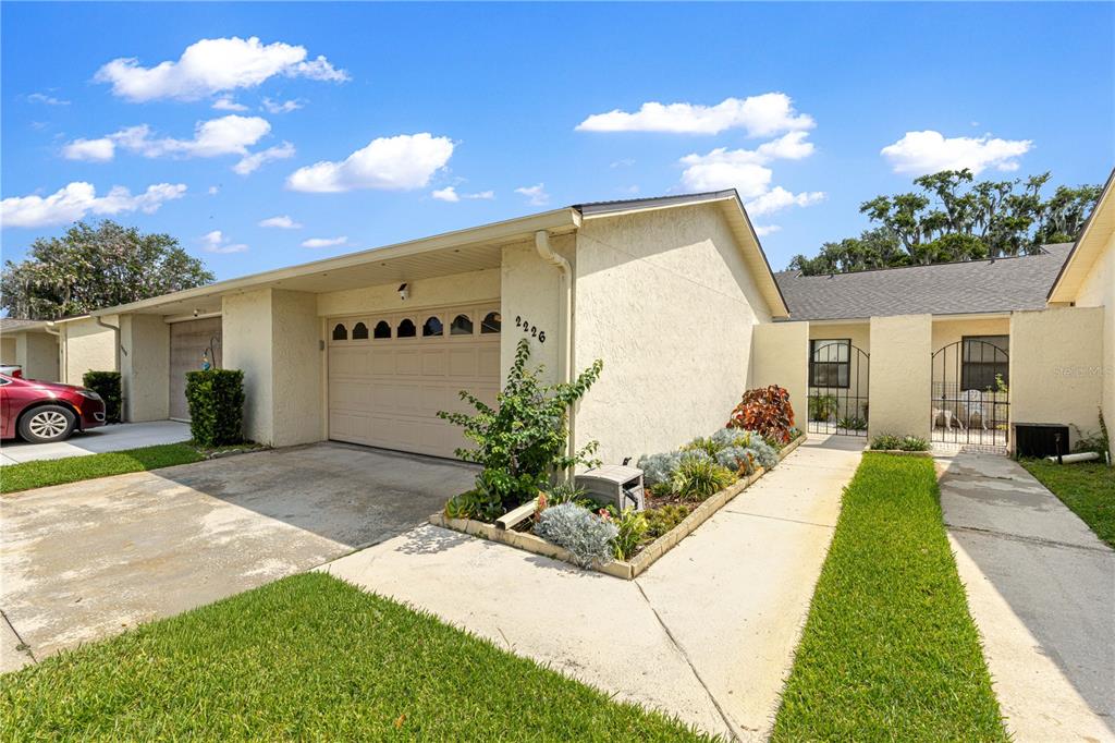 A single-story house exterior features a two-car garage, a concrete driveway, and a landscaped yard — 2226 CYPRESS COVE DRIVE UNIT 2226, TAVARES, FL