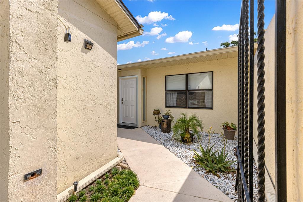 A concrete walkway leads to a white front door in a stucco-walled courtyard with landscaping — 2226 CYPRESS COVE DRIVE UNIT 2226, TAVARES, FL