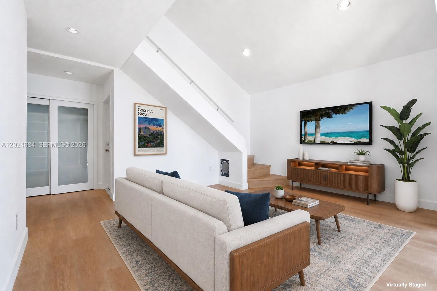 A living room features a sofa, coffee table, media console, and stairs under a slanted ceiling — 3114 Bird Ave # 3114, Miami FL 33133, MIAMI, FL