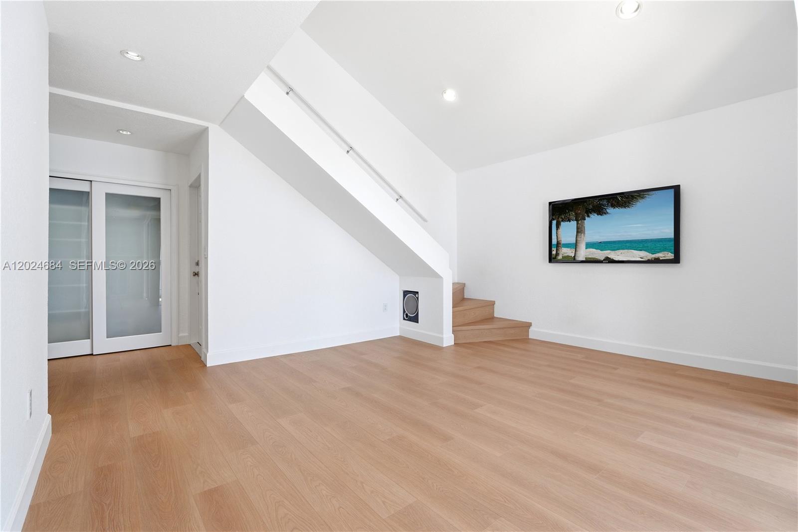 A minimalist room features light wood flooring, white walls, a staircase, and a wall-mounted television — 3114 Bird Ave # 3114, Miami FL 33133, MIAMI, FL