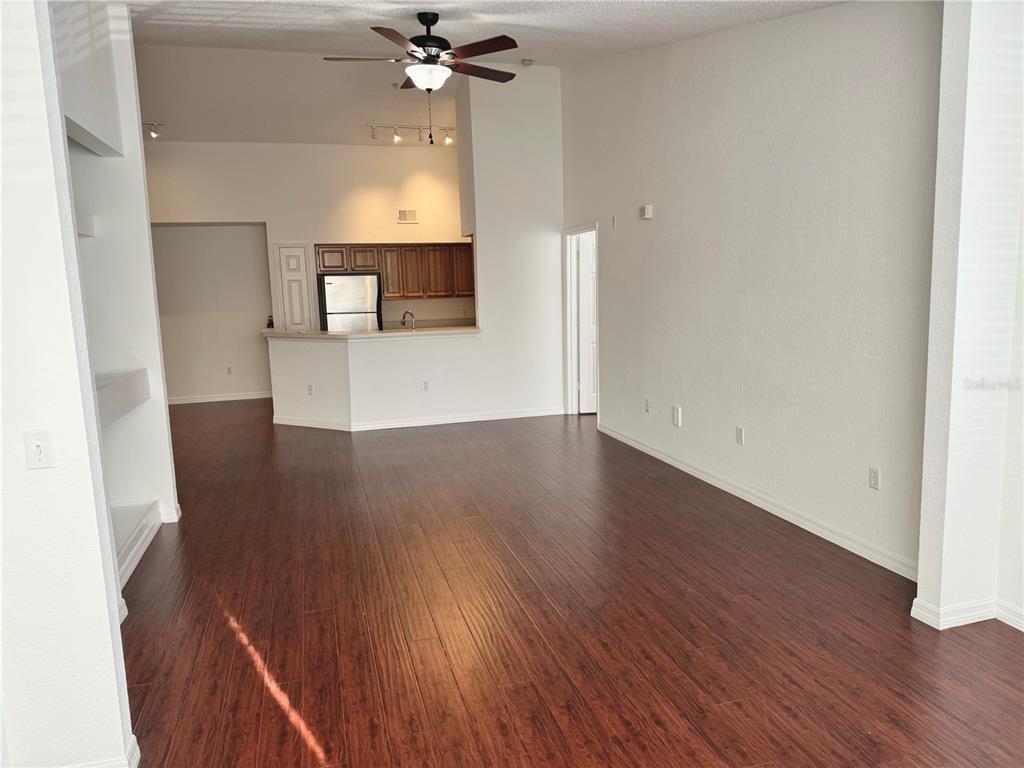 A living room with dark wood-look flooring, a ceiling fan, and an open kitchen area — 13028 PLANTATION PARK CIRCLE UNIT 1226, ORLANDO, FL