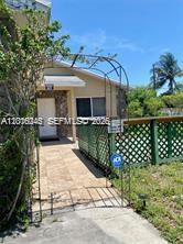 A metal garden archway stands over a stone walkway leading to a house entrance — 2345 Douglas St # 0, Hollywood FL 33020, HOLLYWOOD, FL