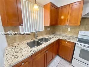 A kitchen features wood cabinets, granite countertops, a double sink, and a white stove — 2345 Douglas St # 0, Hollywood FL 33020, HOLLYWOOD, FL