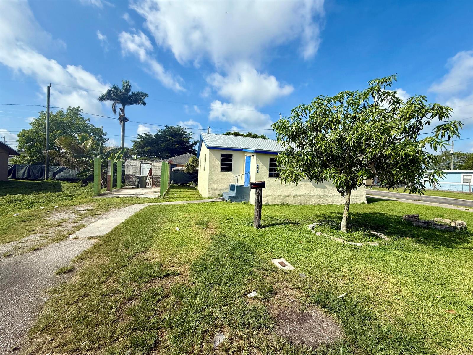 A small, yellow, single-story house with a blue door and a tree in the yard — 856 SW Ave D, Belle Glade FL 33430, BELLE GLADE, FL