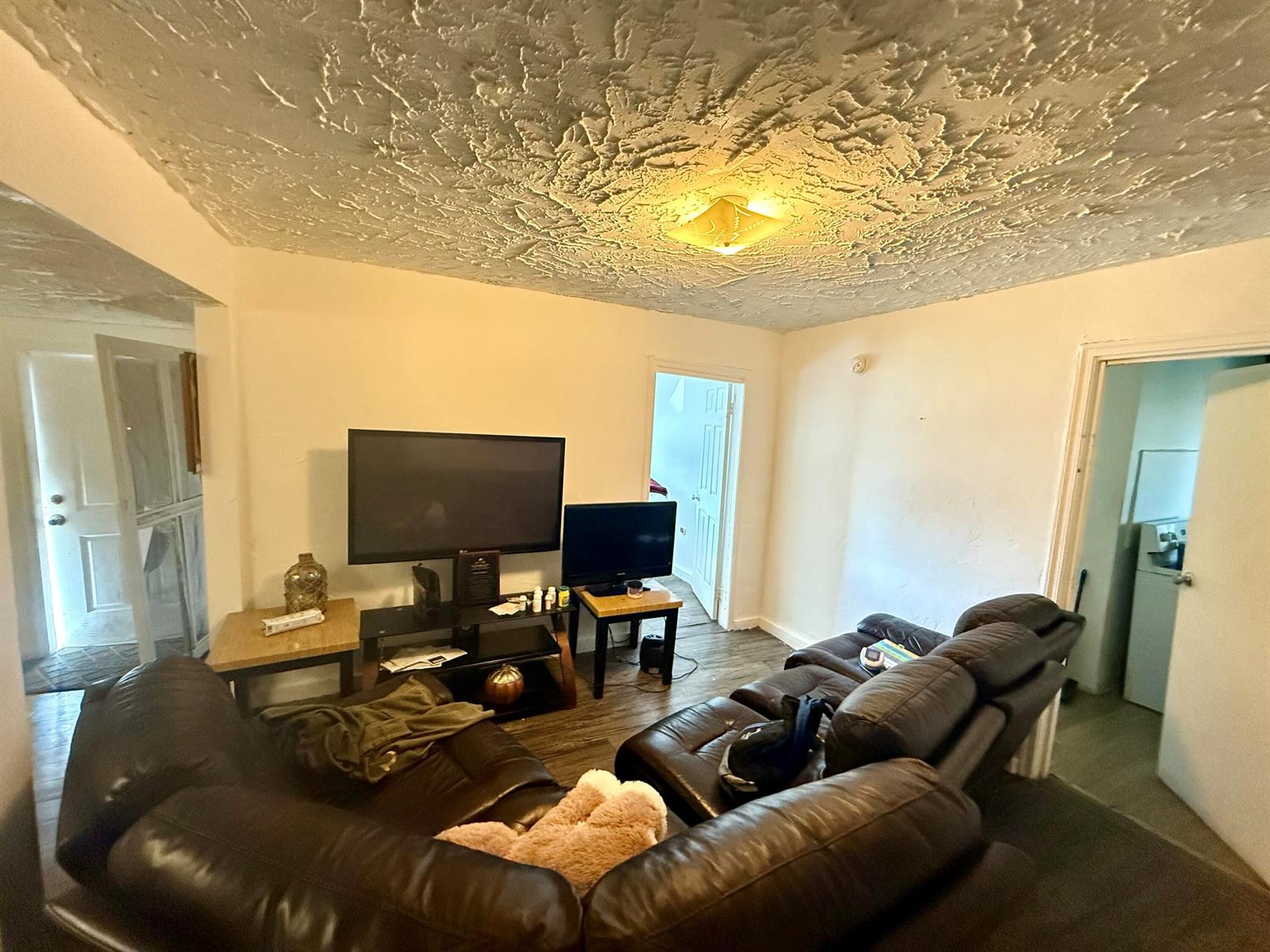 A living room features a dark leather sectional sofa, a television stand, and a textured ceiling — 856 SW Ave D, Belle Glade FL 33430, BELLE GLADE, FL