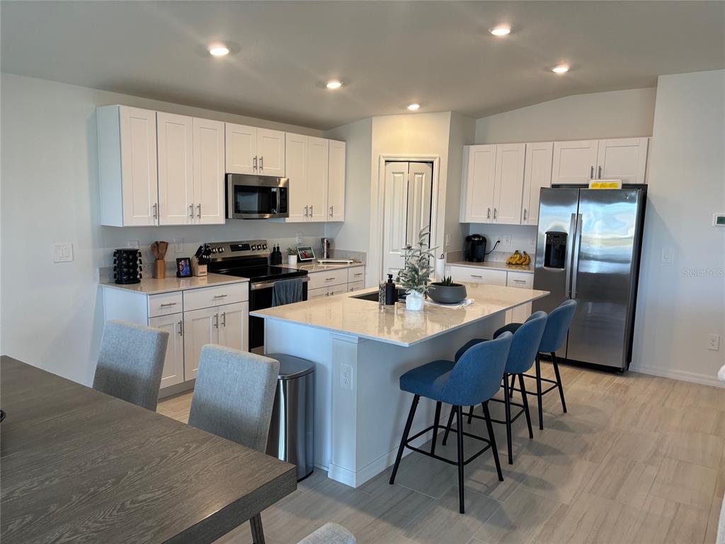 A kitchen features white cabinets, stainless steel appliances, a center island, and blue bar stools — 8823 SUNSET PARK TRAIL, PARRISH, FL