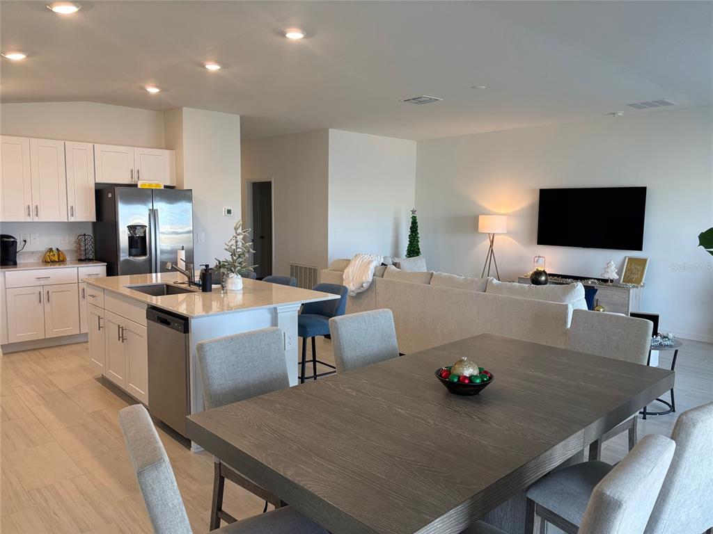 An open-concept kitchen and dining area features white cabinets, a large island, and neutral furniture — 8823 SUNSET PARK TRAIL, PARRISH, FL