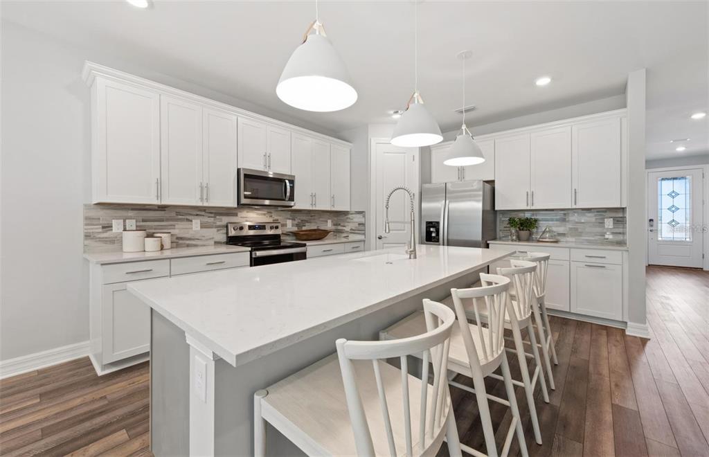An open-concept living room and kitchen featuring gray flooring, white cabinetry, and a sectional sofa — 7433 SUMMER COURT, SARASOTA, FL