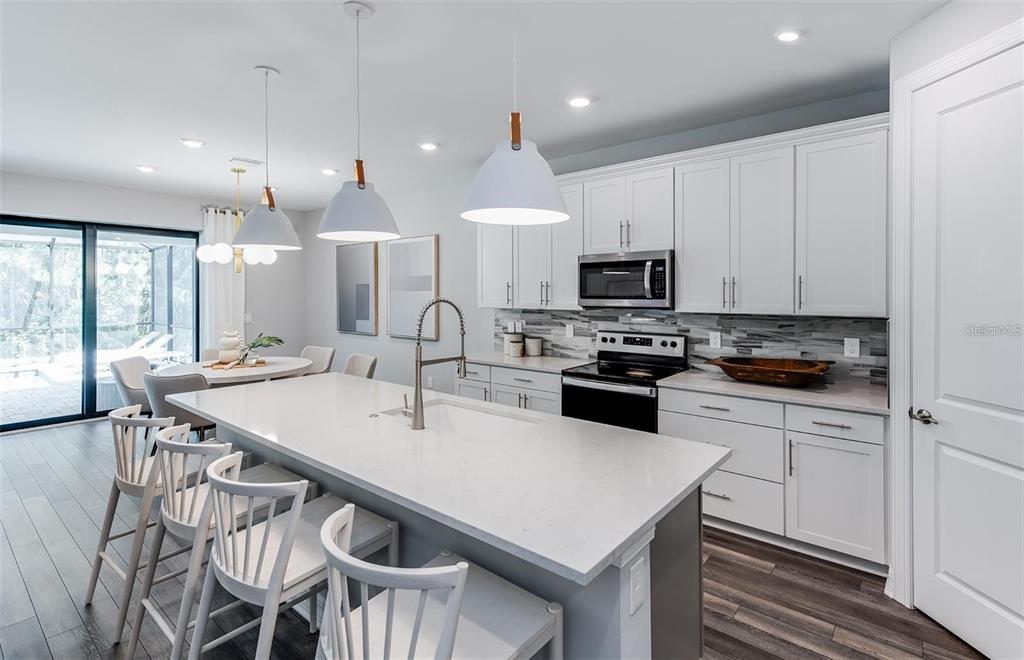 A modern kitchen features white upper cabinets, gray lower cabinets, and a large quartz island — 7433 SUMMER COURT, SARASOTA, FL