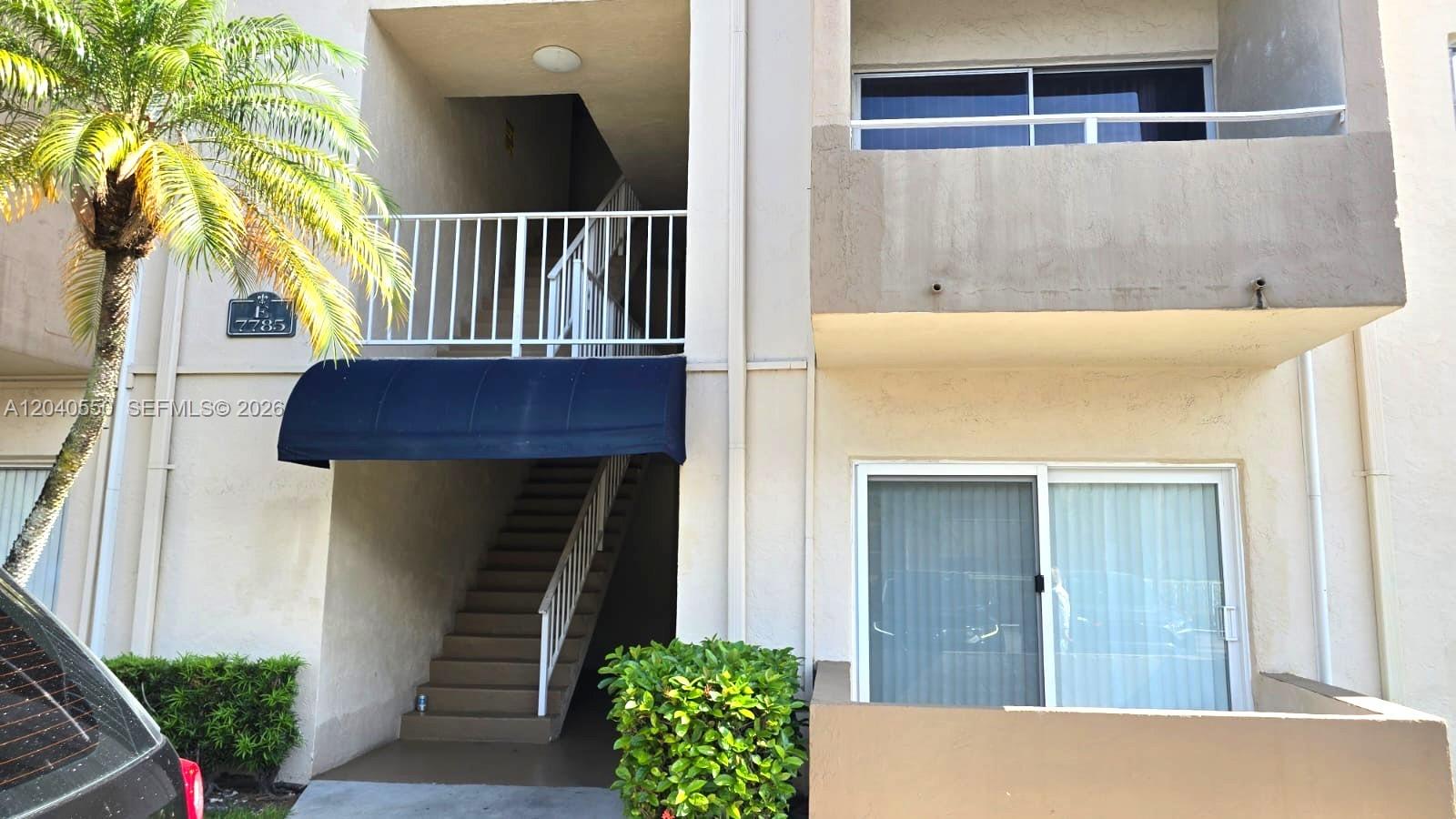An exterior view of a multi-story apartment building with stairs, a balcony, and landscaping — 7785 SW 86th St # 113, Miami FL 33143, MIAMI, FL