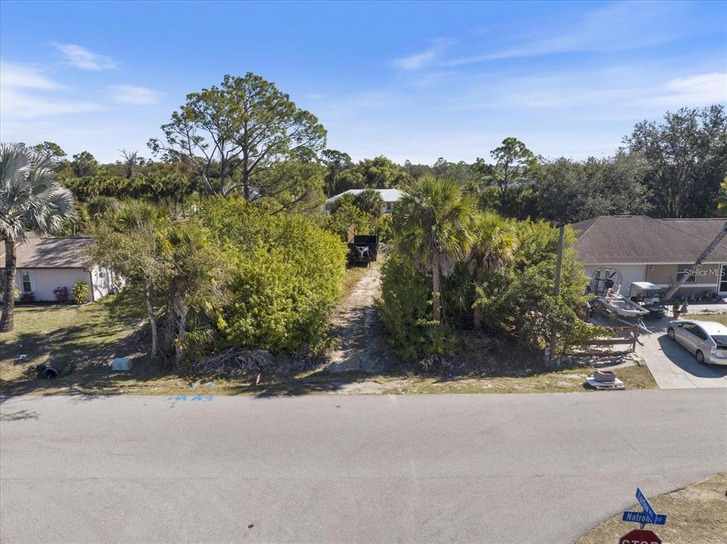An empty, overgrown residential lot sits between two houses on a paved street — NATRONA DRIVE, NORTH PORT, FL