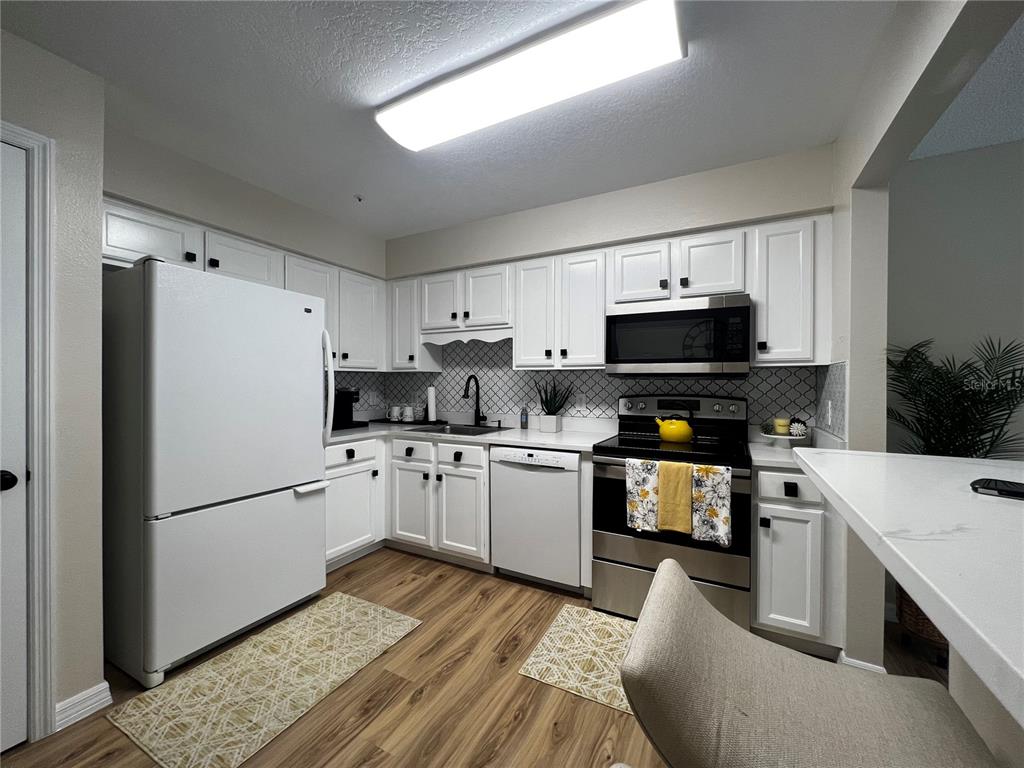 A kitchen features white cabinets, stainless steel appliances, a patterned backsplash, and wood-look flooring — 821 LOCH CALDER UNIT 27, APOPKA, FL