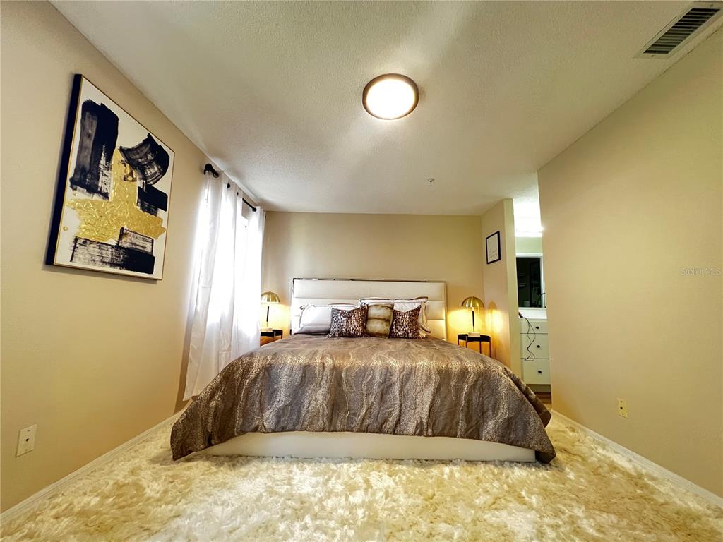 A bedroom features a bed with a metallic comforter, a shaggy rug, and wall art — 821 LOCH CALDER UNIT 27, APOPKA, FL