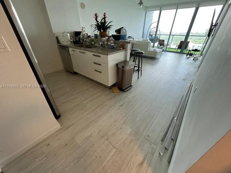 A modern kitchen with white cabinets and light wood-look flooring opens into a living area — 601 NE 36th St # 1305, Miami FL 33137, MIAMI, FL