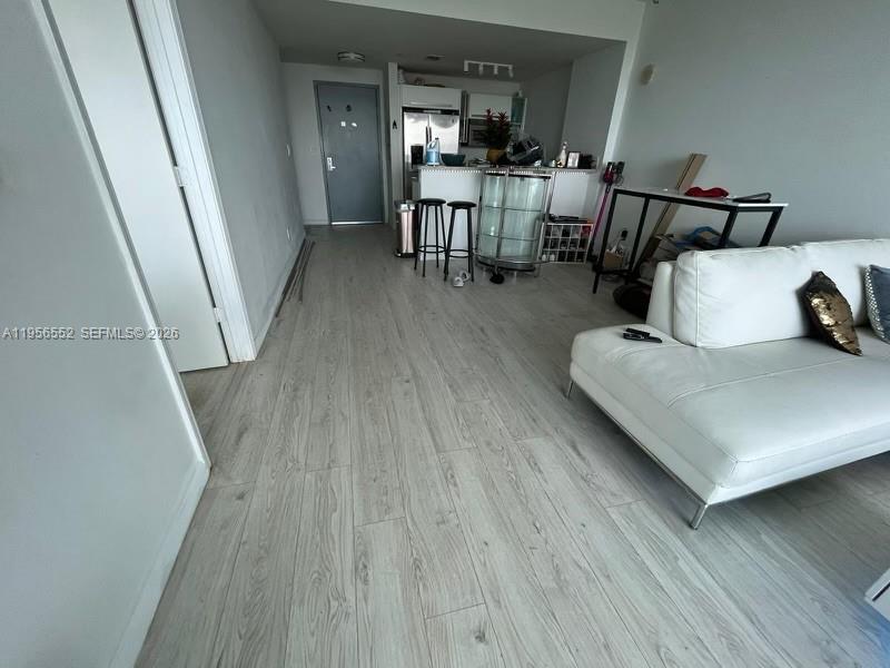 A living room features light wood-look flooring, a white sofa, and an open kitchen area — 601 NE 36th St # 1305, Miami FL 33137, MIAMI, FL