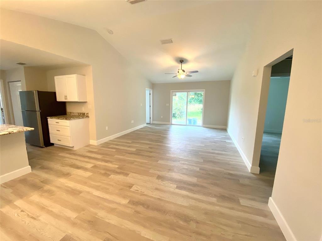 An open-concept living area features light wood-look flooring, a ceiling fan, and a kitchen corner — 8555 NW 210TH STREET, MICANOPY, FL