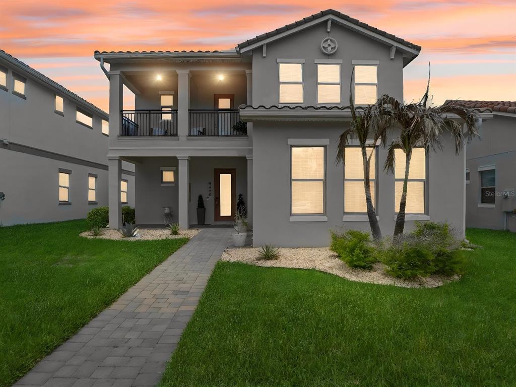 A two-story gray house with a front balcony, stone walkway, and manicured lawn at sunset — 9448 MERE PARKWAY, ORLANDO, FL