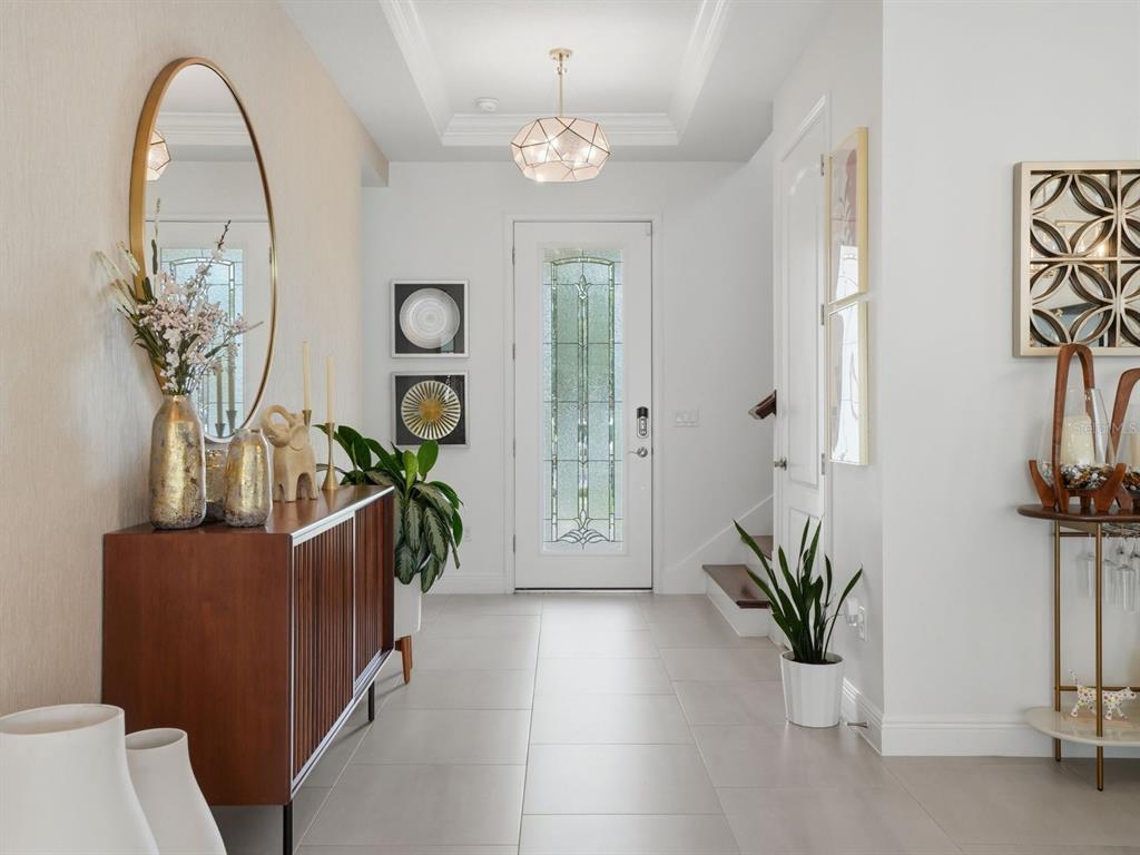A bright foyer features a wooden console table, a round mirror, and a glass-paneled front door — 9448 MERE PARKWAY, ORLANDO, FL