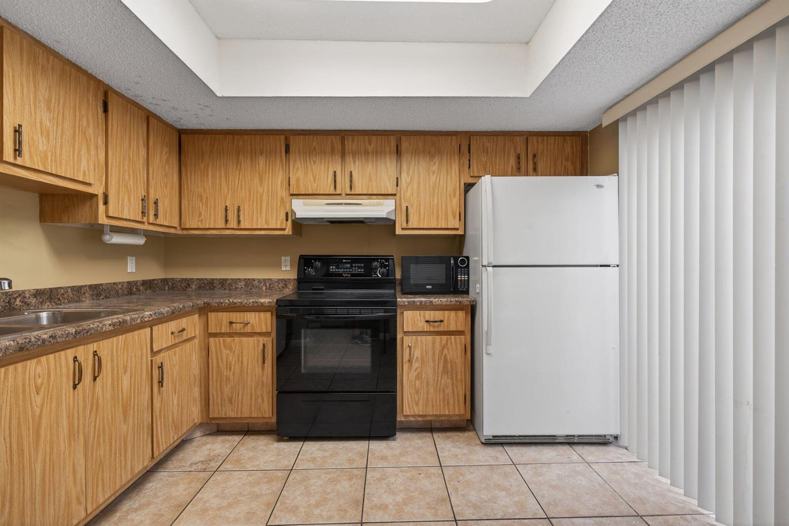 A kitchen features oak cabinets, laminate countertops, black appliances, and a white refrigerator — 707 Stonewood Court # 19c, Jupiter FL 33458, JUPITER, FL