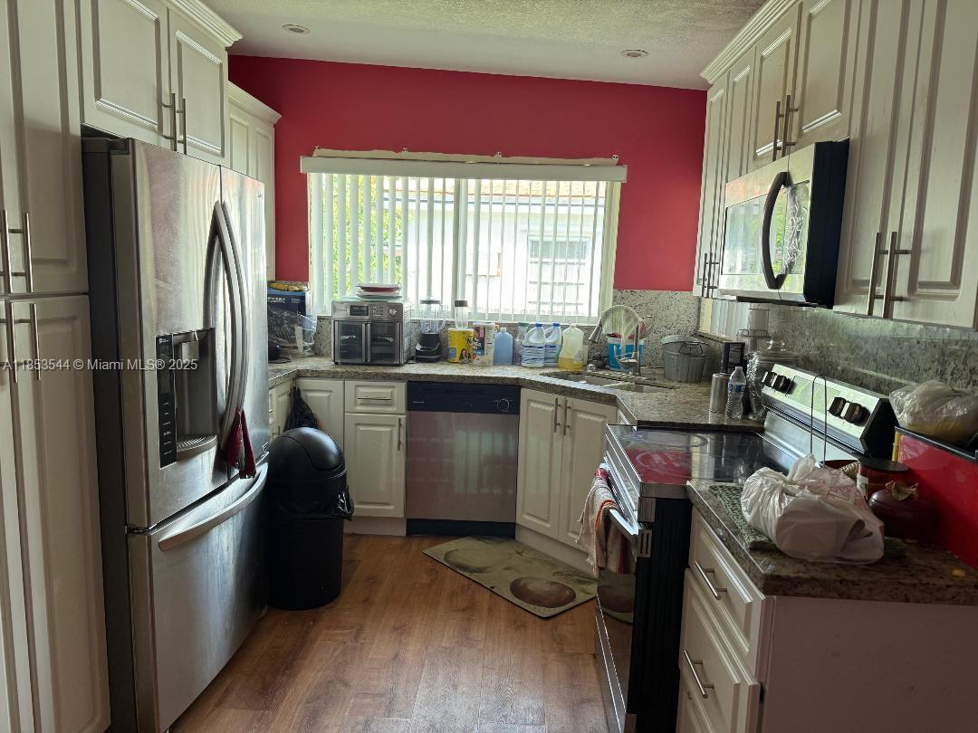 A kitchen features white cabinetry, stainless steel appliances, granite countertops, and a red accent wall — 985 NE 146th St, North Miami FL 33161, NORTH MIAMI, FL