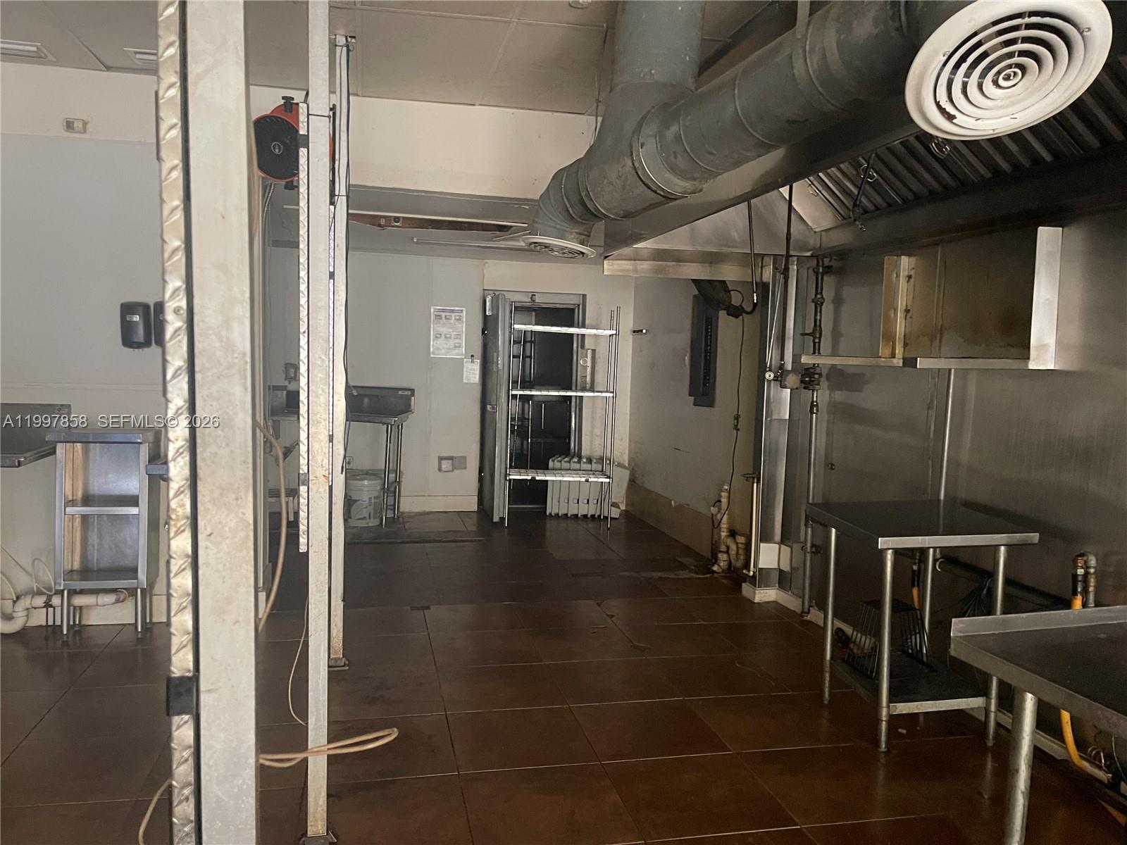 A commercial kitchen features stainless steel prep tables, a ventilation hood, and tiled flooring — 1777 SW 3 AV, Miami FL 33129, MIAMI, FL