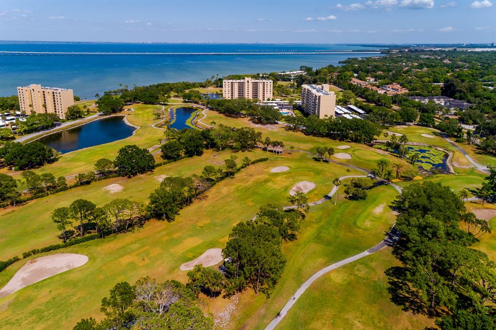 An aerial view shows a golf course with ponds, trees, and several multi-story apartment buildings — 2620 COVE CAY DRIVE UNIT 904, CLEARWATER, FL
