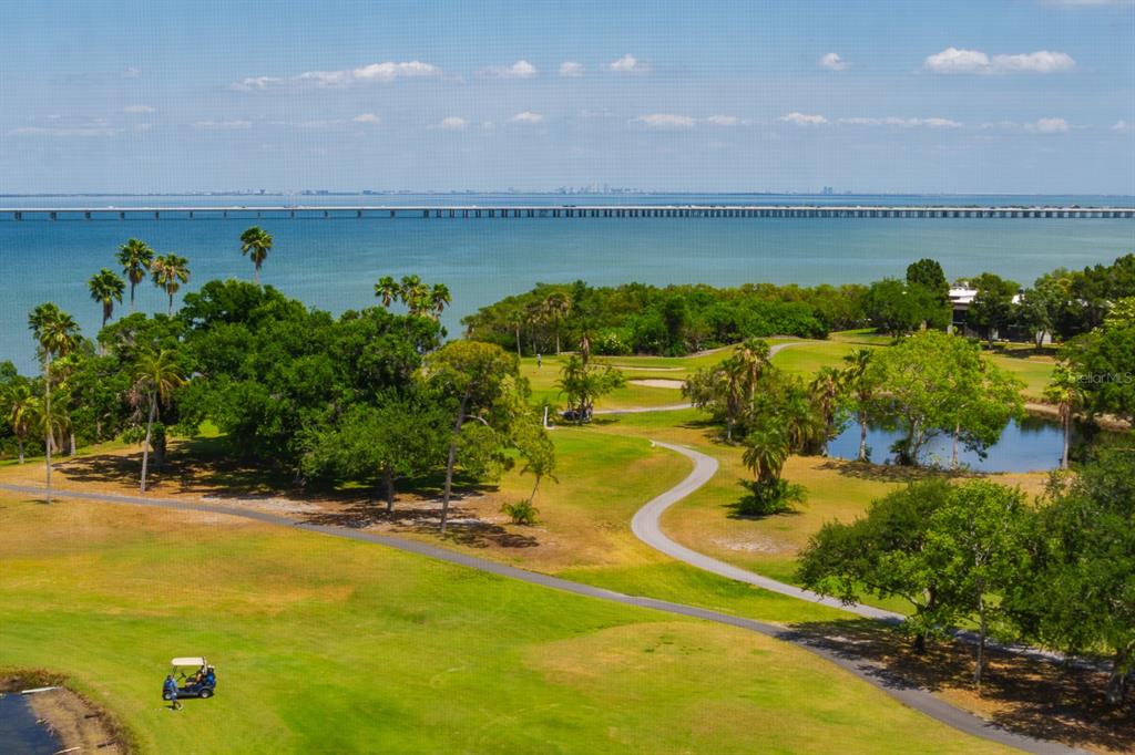 An aerial view of a golf course with a pond, palm trees, and a distant bridge — 2620 COVE CAY DRIVE UNIT 904, CLEARWATER, FL