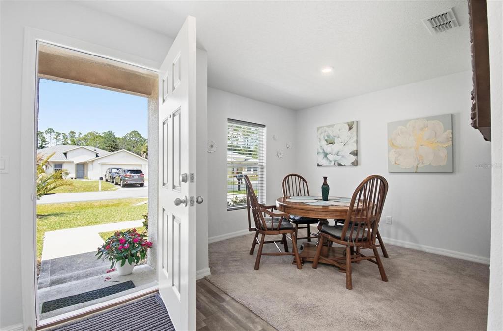A dining area with carpet, a round wooden table, and an open door to the outside — 8 POST OAK LANE, PALM COAST, FL