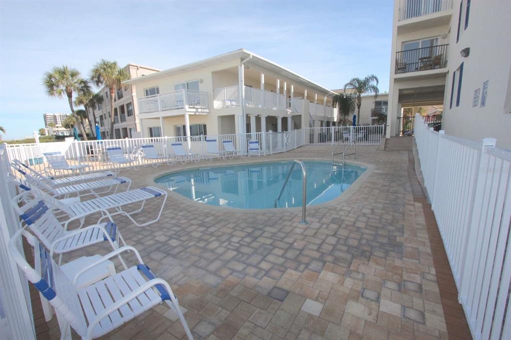 A swimming pool surrounded by lounge chairs and a white fence at a multi-story building — 3200 GULF BOULEVARD UNIT 201, BELLEAIR BEACH, FL