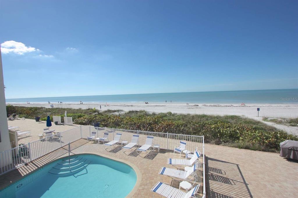 An elevated view of a swimming pool and lounge chairs overlooking a sandy beach — 3200 GULF BOULEVARD UNIT 201, BELLEAIR BEACH, FL
