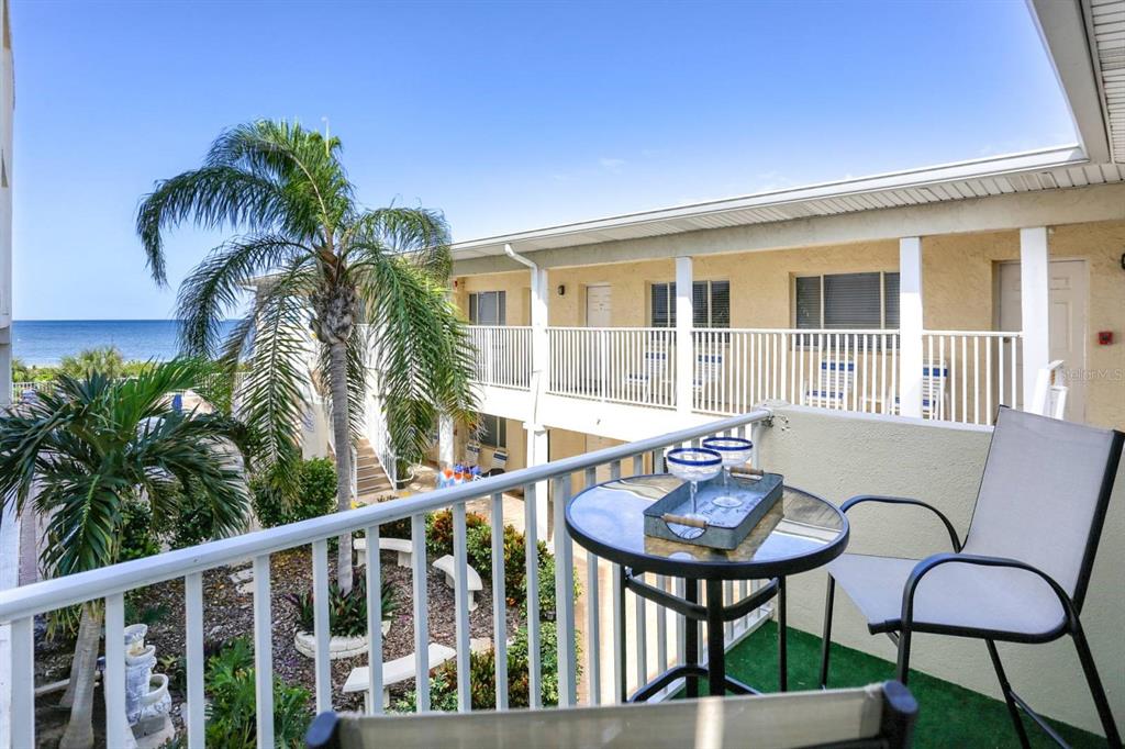 A balcony with a small table and chairs overlooks a courtyard and the ocean — 3200 GULF BOULEVARD UNIT 201, BELLEAIR BEACH, FL