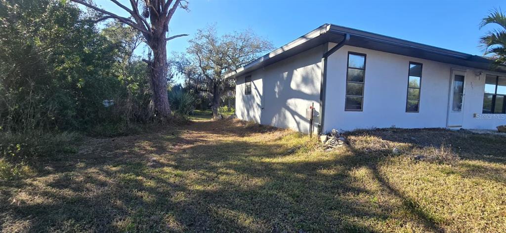 A side view of a white, single-story house with a yard and large trees — 525 ALTOONA STREET NW, PORT CHARLOTTE, FL