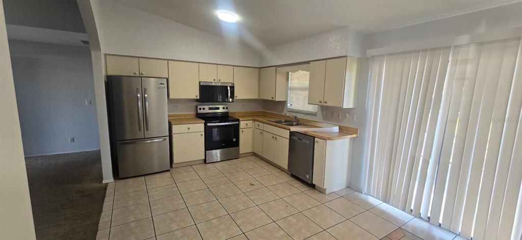 A kitchen features light-colored cabinets, stainless steel appliances, tile flooring, and a sliding glass door — 525 ALTOONA STREET NW, PORT CHARLOTTE, FL