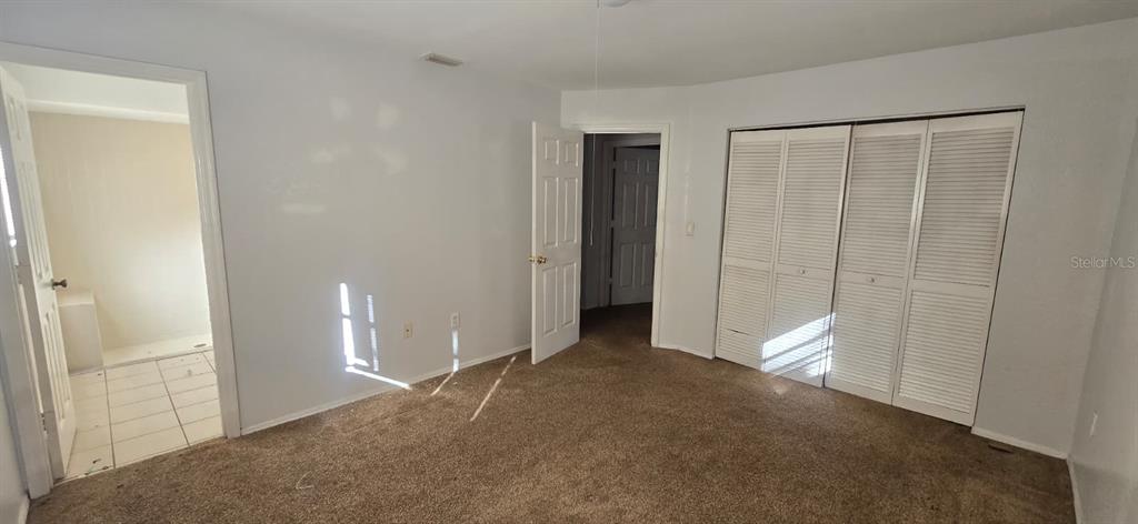 A bedroom with brown carpet, white walls, a closet with louvered doors, and an attached bathroom — 525 ALTOONA STREET NW, PORT CHARLOTTE, FL