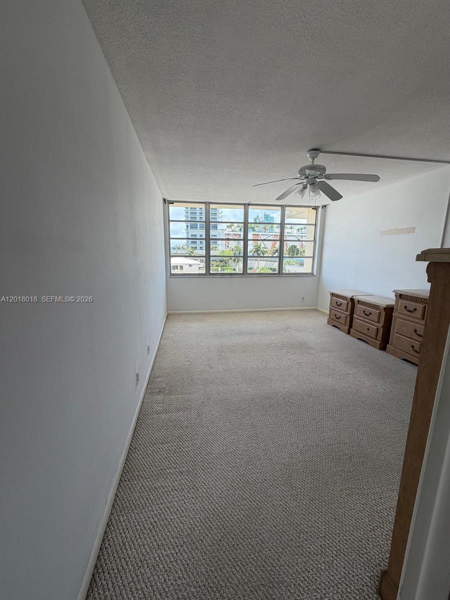A carpeted bedroom features a ceiling fan, white walls, and a large window with city views — 1817 S Ocean Dr # 319, Hallandale Beach FL 33009, HALLANDALE BEACH, FL