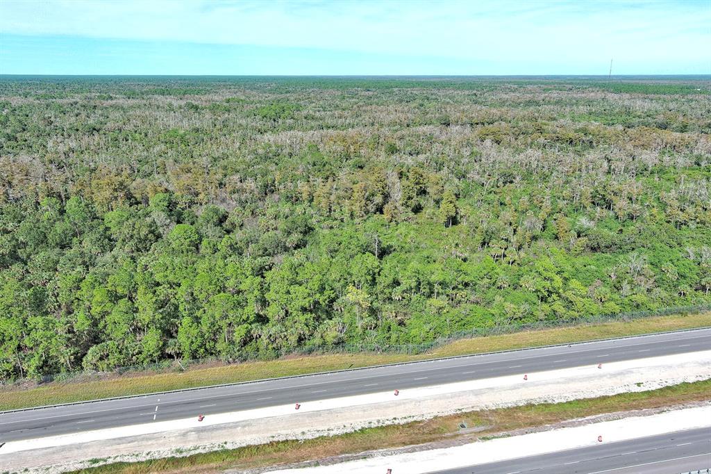An aerial view shows a multi-lane highway bordering a large, dense forest of trees — 4345 42ND AVENUE SE, NAPLES, FL