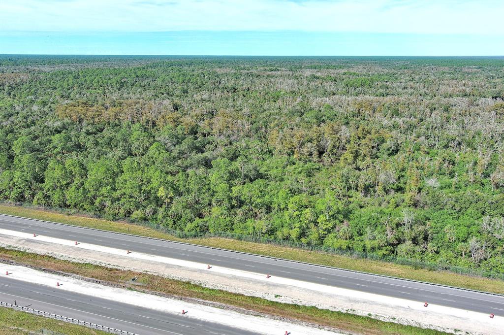 An aerial view shows a multi-lane highway running alongside a large, dense forest — 4345 42ND AVENUE SE, NAPLES, FL