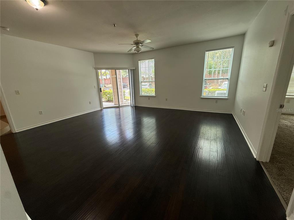 An empty living room features dark wood flooring, a ceiling fan, and sliding glass doors — 2015 ERVING CIRCLE UNIT 102, OCOEE, FL