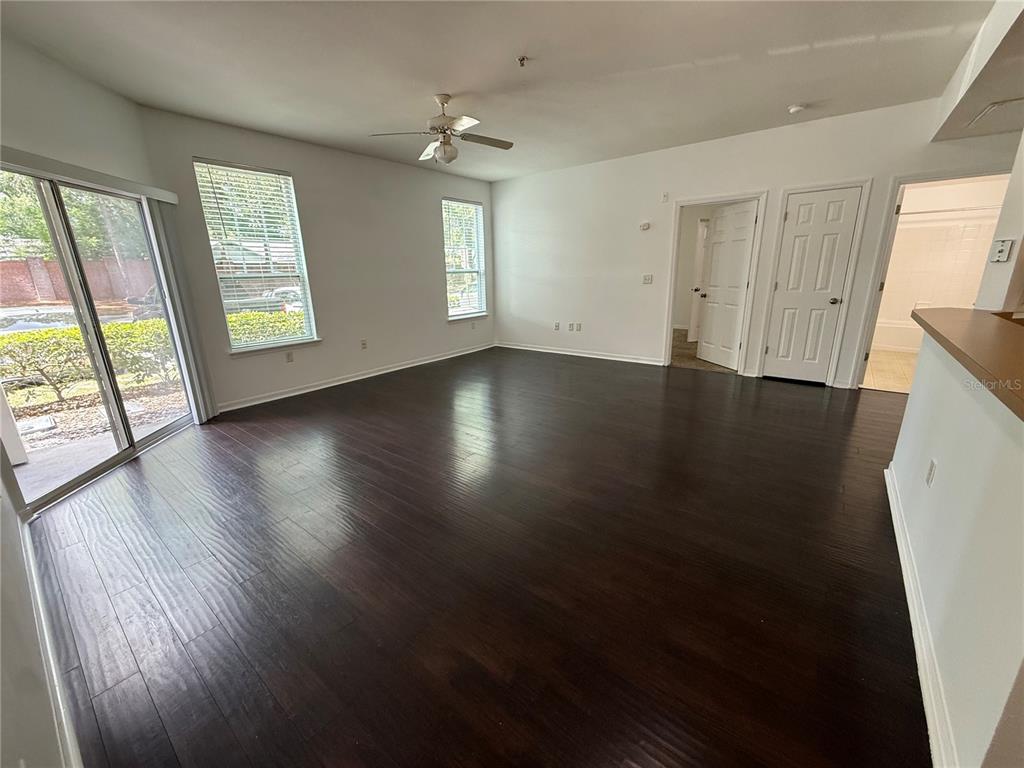 An empty living room features dark wood flooring, a ceiling fan, and sliding glass doors — 2015 ERVING CIRCLE UNIT 102, OCOEE, FL