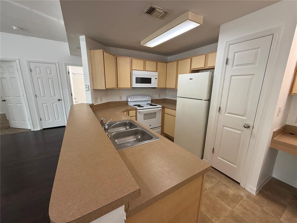 A kitchen features light wood cabinets, white appliances, a double sink, and tan countertops — 2015 ERVING CIRCLE UNIT 102, OCOEE, FL
