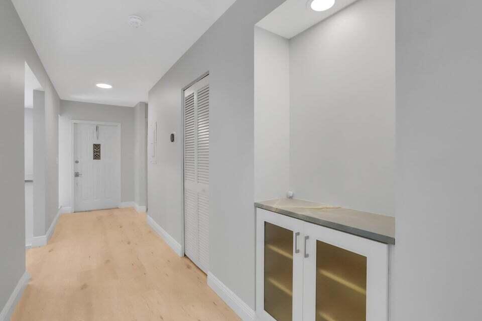 A hallway with light wood flooring, a white door, a louvered closet, and built-in cabinetry — 3113 Kingswood Terrace, Boca Raton FL 33431, BOCA RATON, FL