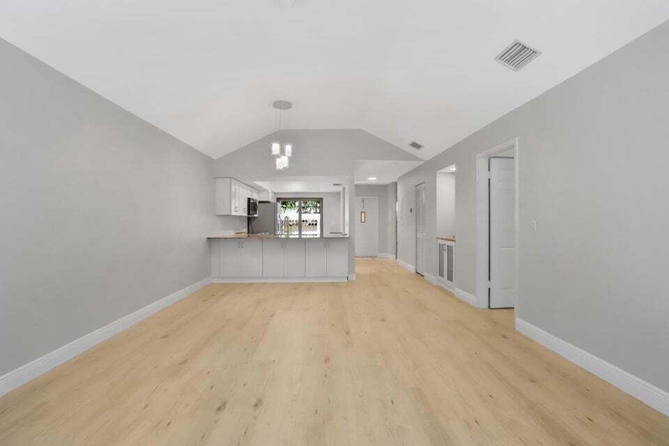 A spacious room with light wood flooring, gray walls, and an open kitchen with white cabinets — 3113 Kingswood Terrace, Boca Raton FL 33431, BOCA RATON, FL
