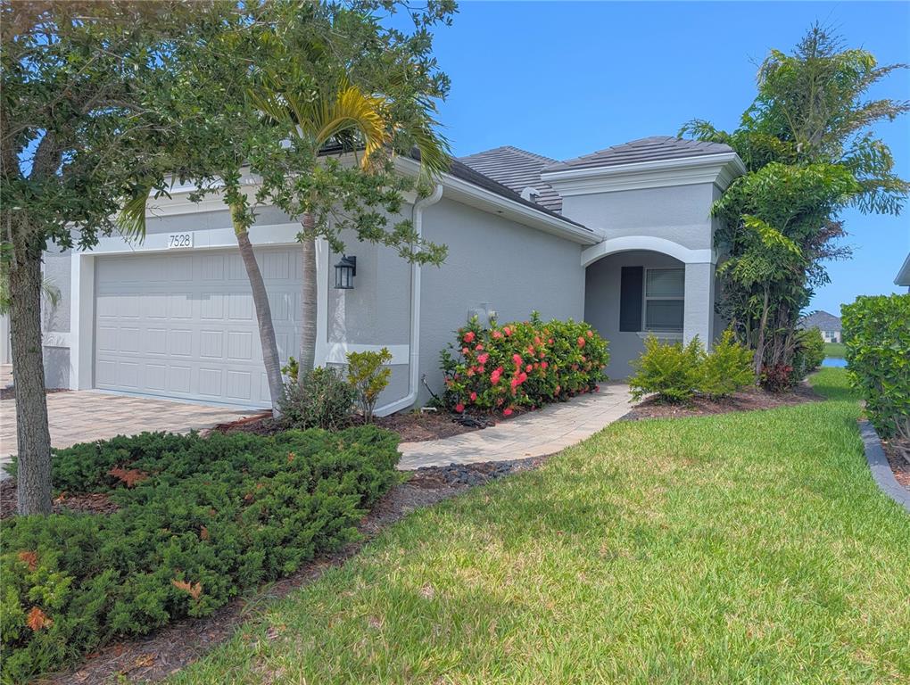 A single-story house with a gray stucco exterior, a two-car garage, and a paved walkway — 7528 ALUMNI TRAIL, SARASOTA, FL