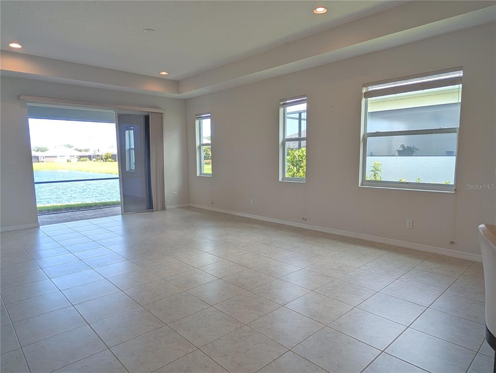 An empty living room with tile floors, recessed lighting, and a sliding door to a lake — 7528 ALUMNI TRAIL, SARASOTA, FL