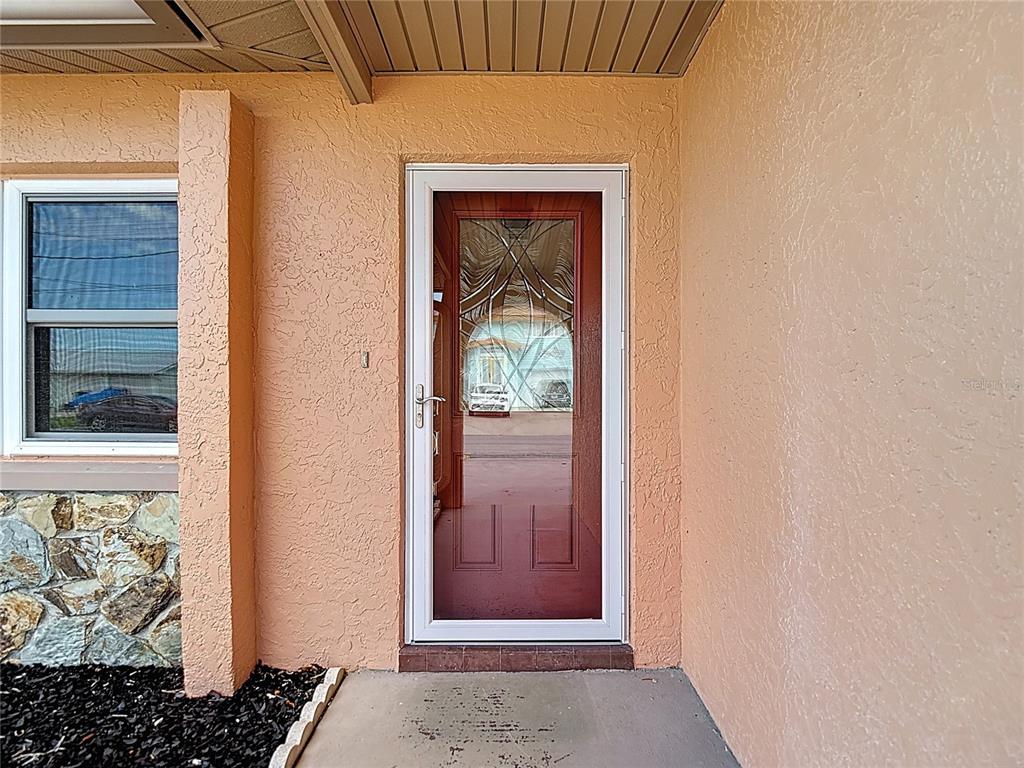 A white storm door with decorative glass panels is set into a peach-colored stucco wall — 13816 VICTOR AVENUE, HUDSON, FL