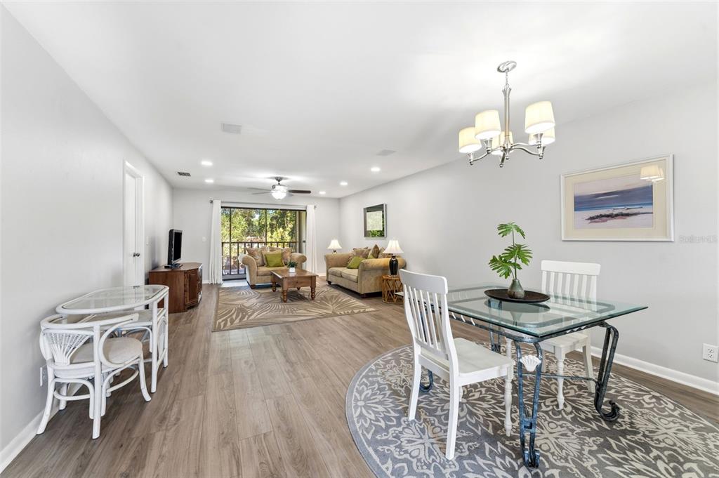 An open-concept living and dining area features light wood flooring and a glass-topped dining table — 101 LAKE AVENUE NE UNIT 215, LARGO, FL