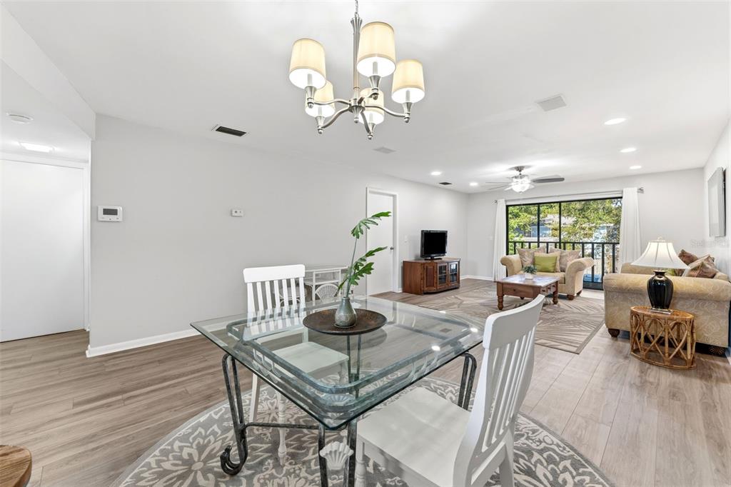 A dining area with a glass table and white chairs opens into a living room — 101 LAKE AVENUE NE UNIT 215, LARGO, FL